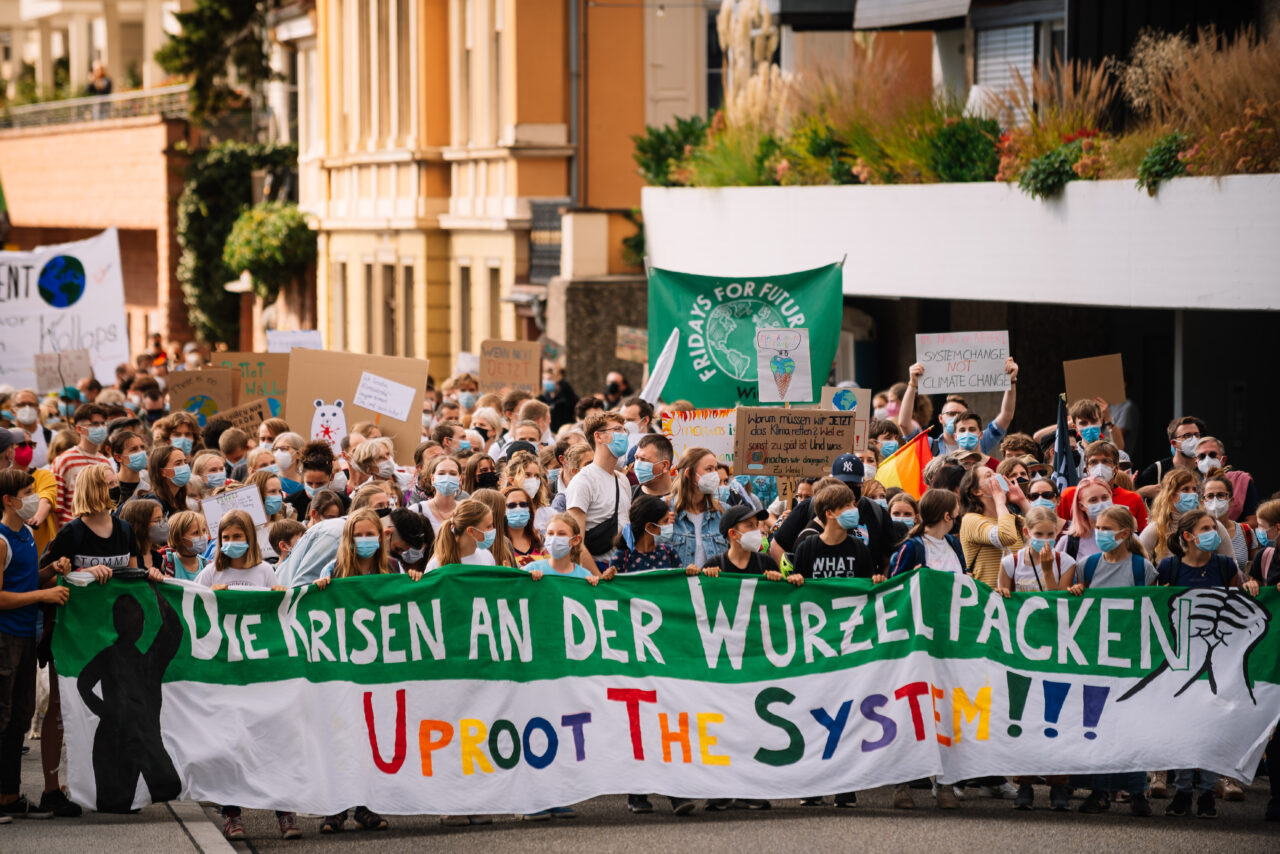 Bild vom Streik am 24.09.2021, zu sehen ist der Beginn des Demozuges auf der Neuenheimer Landstraße und das Frontbanner mit der Aufschrift "Die Krisen an der Wurzel packen, Uproot the System !!!"