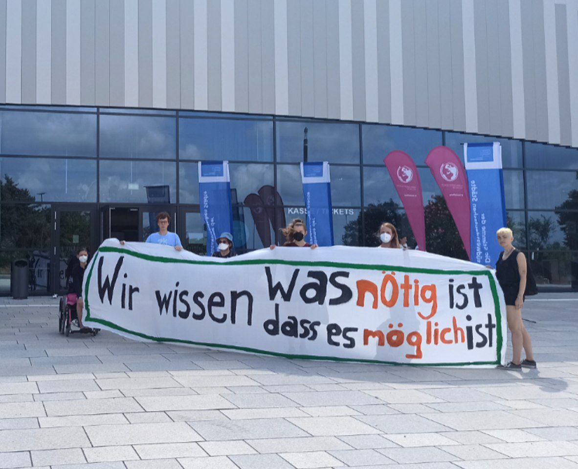 Sechs Fridays for Future Aktivist*innen stehen vor dem Veranstaltungsort des Städtetages BW, dem SNP Dome in Heidelberg. Sie halten ein Banner mit der Aufschrift "Wir wissen was möglich ist und wir wissen dass es möglich ist" hoch.